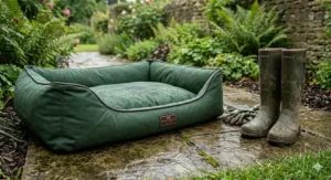 A green waterproof canvas dog bed placed on a patio flagstone path next to a pair of muddy wellington boots.